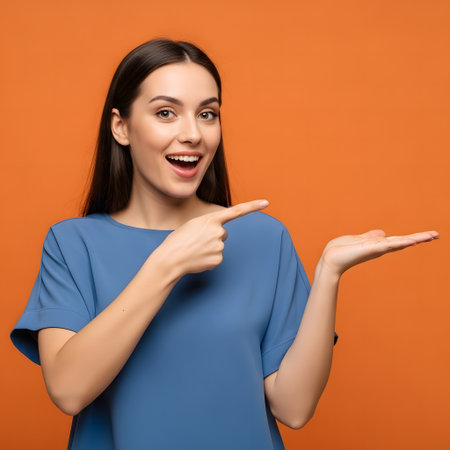 Portrait of a happy young woman pointing at copy space on orange backgroundの素材