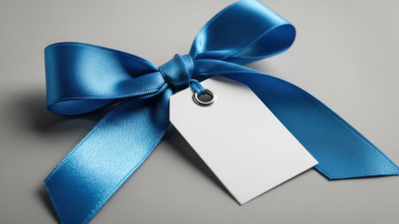 A close-up image of a beautifully tied blue ribbon with a white tag attached to it. The ribbon is neatly arranged with a small silver ring holding it together. The tag is blank, ready for a personalized message.の素材