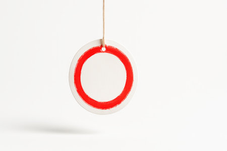 Floating white cardstock circle tag with vermilion dry brush halo around the edge thin cotton string above clean retail branding mockup on whiteの素材