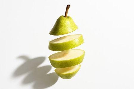 Whole pear with thin slices levitating in a loose vertical spiral on whiteの素材