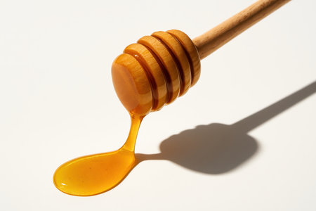 Wooden honey dipper at a forty five degree angle with a long viscous thread poolingの素材