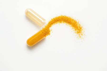Dried turmeric powder capsule opened with golden powder spilling in a clean arc studio isolated on whiteの素材