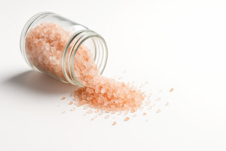 Himalayan pink salt in a clear glass jar tipped slightly with a clean trail of crystals fanning outward on whiteの素材