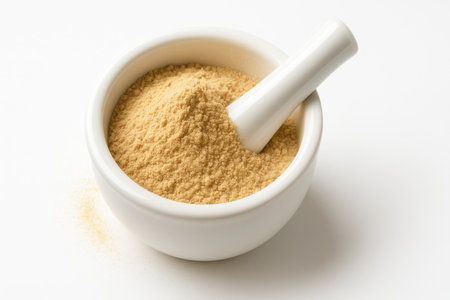 White ceramic mortar filled with maca root powder with a pestle partly embedded and a light dust haze around the rim clean wellness visualの素材