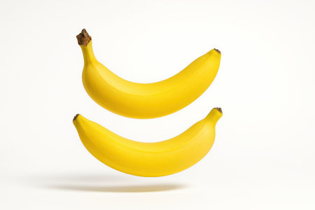 Two ripe yellow bananas captured in gentle mid air levitation slightly offset with a faint shadow ellipse clean studio on whiteの素材