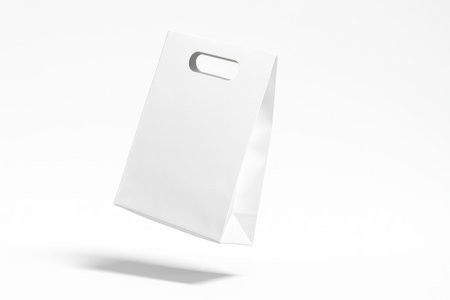 Blank white paper bag with die cut handle on pure white suspended mid air with a slight tilt showing handle slot thickness and side profileの素材