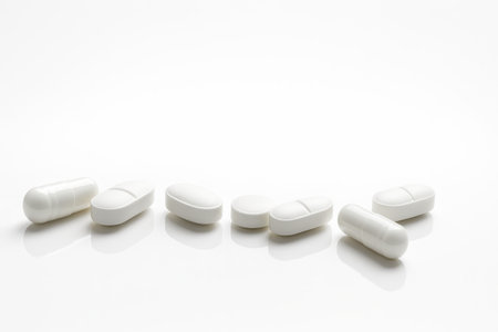 Scattered row of white pills and capsules glossy acrylic creates a faint mirror reflection beneath a curved s shaped rowの素材