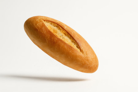Traditional Turkish bread somun ekmek mid air with a light dust of flour falling around the loaf on whiteの素材