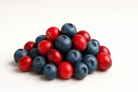 Cranberries and blueberries with green leaves on white background side view wide pile arranged in gentle slope for fruit snack and healthy diet themesの素材