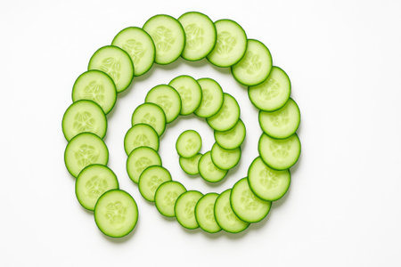 Fresh cucumber slices arranged in flowing spiral from center on white background top down for salad ingredient healthy diet and food styling themesの素材