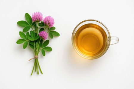 Top down professional photograph of fresh clover bouquet tied with string beside glass cup of herbal tea on white background natural wellness concept for organic drink and healing designの素材