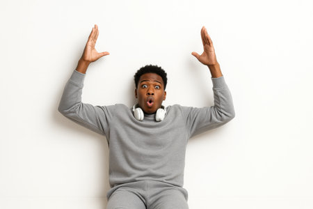 Top view of astonished dark skinned young man lying on white studio floor in sweatshirt and joggers expressive surprise portrait for reaction meme and lifestyle designの素材