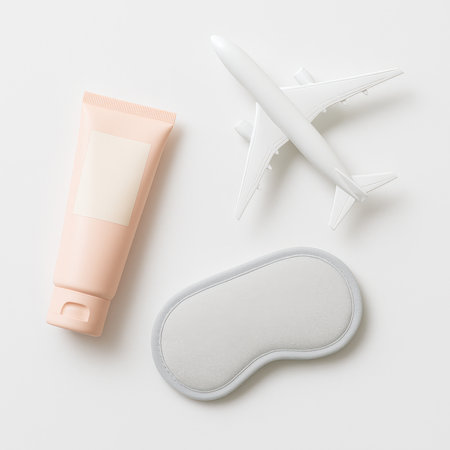 Slim pastel plastic lotion tube with blank label lying diagonally on white surface with small airplane model and sleep maskの素材