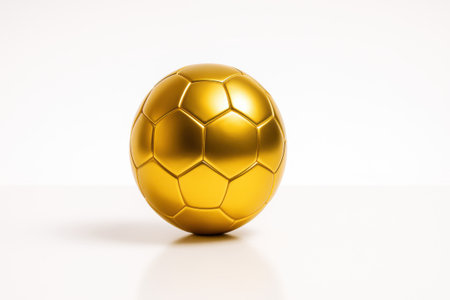 Shiny golden soccer ball standing alone on glossy white surface isolated on pure white background with gentle reflectionの素材