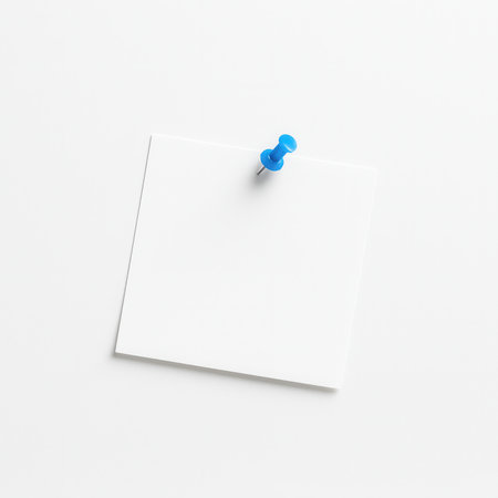 Top view blank white paper note pinned with small blue pushpin slightly off center on seamless white backgroundの素材