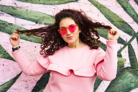 Long haired curly brunette woman in pink dress and pink glasses looks fun with a squint.の写真素材