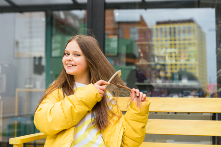 A long-haired, cheerful blonde girl combs her hair with a comb and laughs carelessly. Bright pink background. Place for textの写真素材