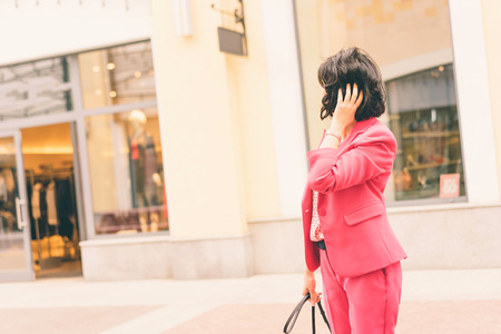 A woman in fashionable clothes  holds in hands with French manicure a black handbag. Shopping mall. Fashion and Shopping conceptの写真素材