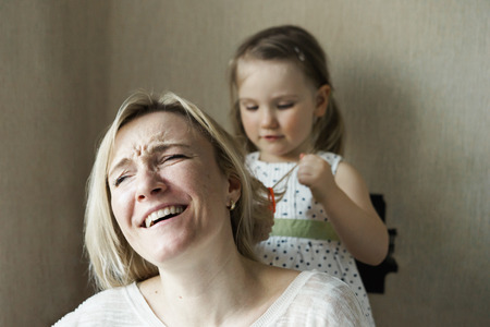 Mom and daughter are sitting by the window, daughter makes mom hairstyle, mother laughsの写真素材