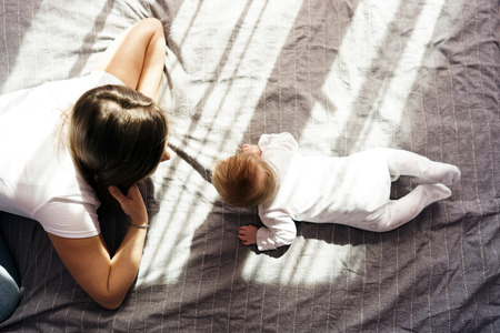 Mother with her newborn son lay on the bed in the rays of sunlight coming out of the window through the curtains. Top viewの写真素材