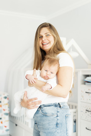 Pretty blond long-heared mom and newborn son in her arms in the white children room. The concept of new life, love and helplessness.の写真素材