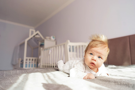 A newborn baby is lying on his stomach in the nursery on the bed. Kid with funny chubchik on his headの写真素材