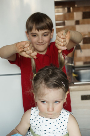Brother and sister in the kitchen and the boy pulls the girl by the tails.の写真素材