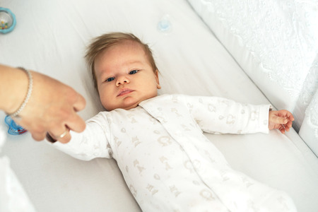 A newborn baby is lying in the nursery on the bed. Mothers hand holds sons hand