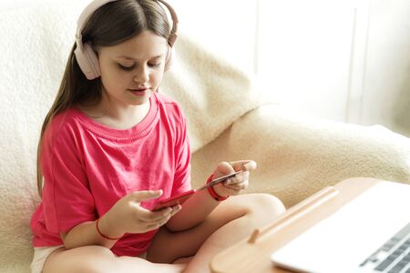 Cheerful girl in pink headphones and a red T-shirt sits with a phone in her hand and a credit card....