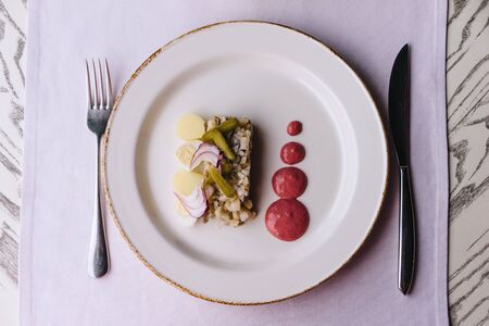 Restaurant delicacy dish on a purple tablecloth. White plate with herring, gherkins, red onions and quail eggs. Farshmak with beetroot sauce.の写真素材