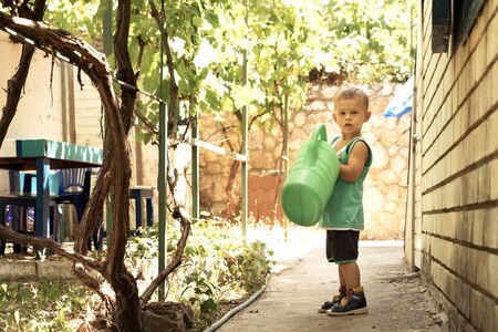 A little boy with a big green watering can is in the yard. Great mothers helper.の写真素材