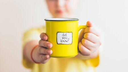 A girl in a yellow T-shirt with a yellow cup in her hand, on which was written Did you know. Interesting fact.の写真素材