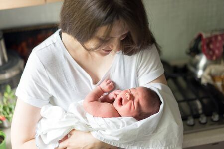 A mother with a newborn baby in her arms is breastfeeding him in the kitchenの写真素材
