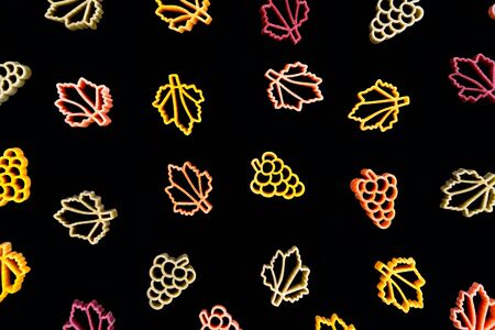 Autumn composition of curly multi-colored Italian pasta in the form of leaves and grapes on a black background. Flat lay. Open compositionの写真素材