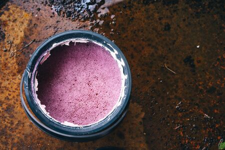 Spoiled white paint in a jar turned into a pink liquid with bubbles standing on a rusty metal surfaceの写真素材