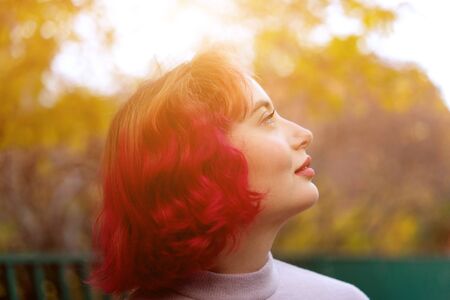Beautiful woman with red dyed hair and background of autumn yellow leaves. Autumn timeの写真素材