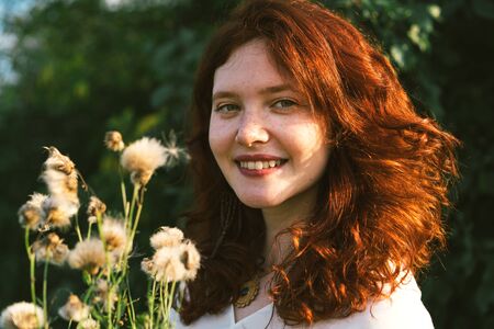 Beautiful young woman with red curly hair and freckles on her face. Close-up portrait with fluffy...