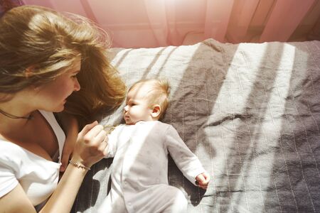 Mother with her newborn son lay on the bed in the rays of sunlight coming out of the window through...
