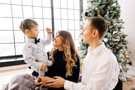 The little boy with his parents near a Christmas tree. Merry Christmas and happy New year concept. Happy family at homeの写真素材