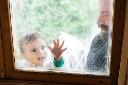 Father and little son are playing together. Dad and child looking through the window. Family weekend...