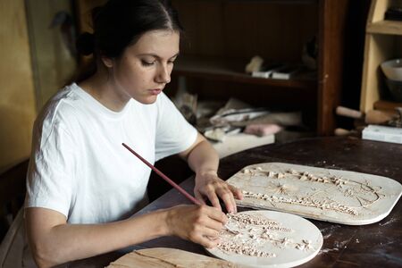 Woman hands brush with a brush the relief pattern obtained from the mold for casting clay products. Shaped method of preparing pottery. Handwork. Ceramic Making. Wall panelの写真素材