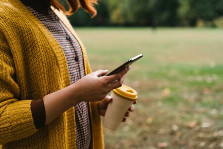 A red-haired woman is walking in the park and holding a bamboo cup with hot coffee in her hand and...