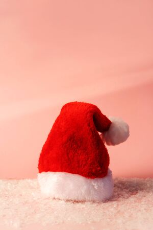 Santa Claus red hat with white fur standing on pastel pink color covered artificial snow background. Funny minimal composition. Happy holiday flat lay layout. New year preparations. Copy spaceの写真素材