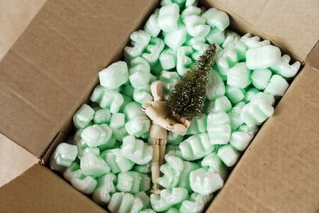 A cardboard box filled with synthetic mint filler for transportation and a figure of a wooden man with an artificial Christmas tree in his hands. Environmental protection concept and Neo eco friendlyの写真素材