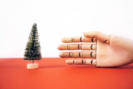 Christmas artificial tree on a wooden stand and a mock up of a hand reaching for a tree. The concept of New Years preparations and sales. Environmental Protection. Zero waste. Minimalist backgroundの写真素材