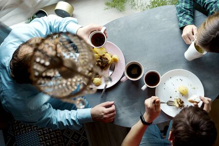 Family breakfast at the oval table by the window. Father and two sons eating potatoes and drinking coffee from white ceramic mugs. Top view through a crystal chandelier. Weekend Family Customs Conceptの写真素材