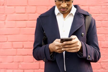 A man in a dark blue jacket is standing in city by red pink wall with a phone in his hands looking for navigation. Solo overseas traveler, sightseeing. Taxi booking by mobile appの写真素材