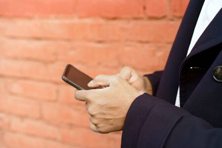 A man in a dark blue jacket is standing in city by red pink wall with a phone in his hands looking...