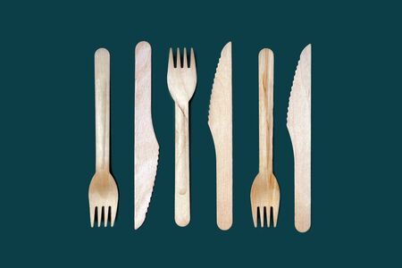 Set of disposable wooden knives and forks on a dark green emerald background. The concept of plastic...