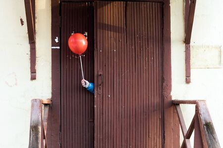 Children's hand in a blue jacket protruding from behind a wooden door with a red ball on a stick. Hide and seek game, children's conceptの写真素材